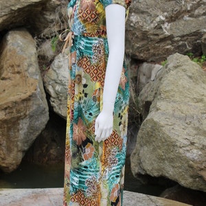 May include: A long, flowing maxi dress with a colorful floral print. The dress has a scoop neck, short sleeves, and a tie at the waist.
