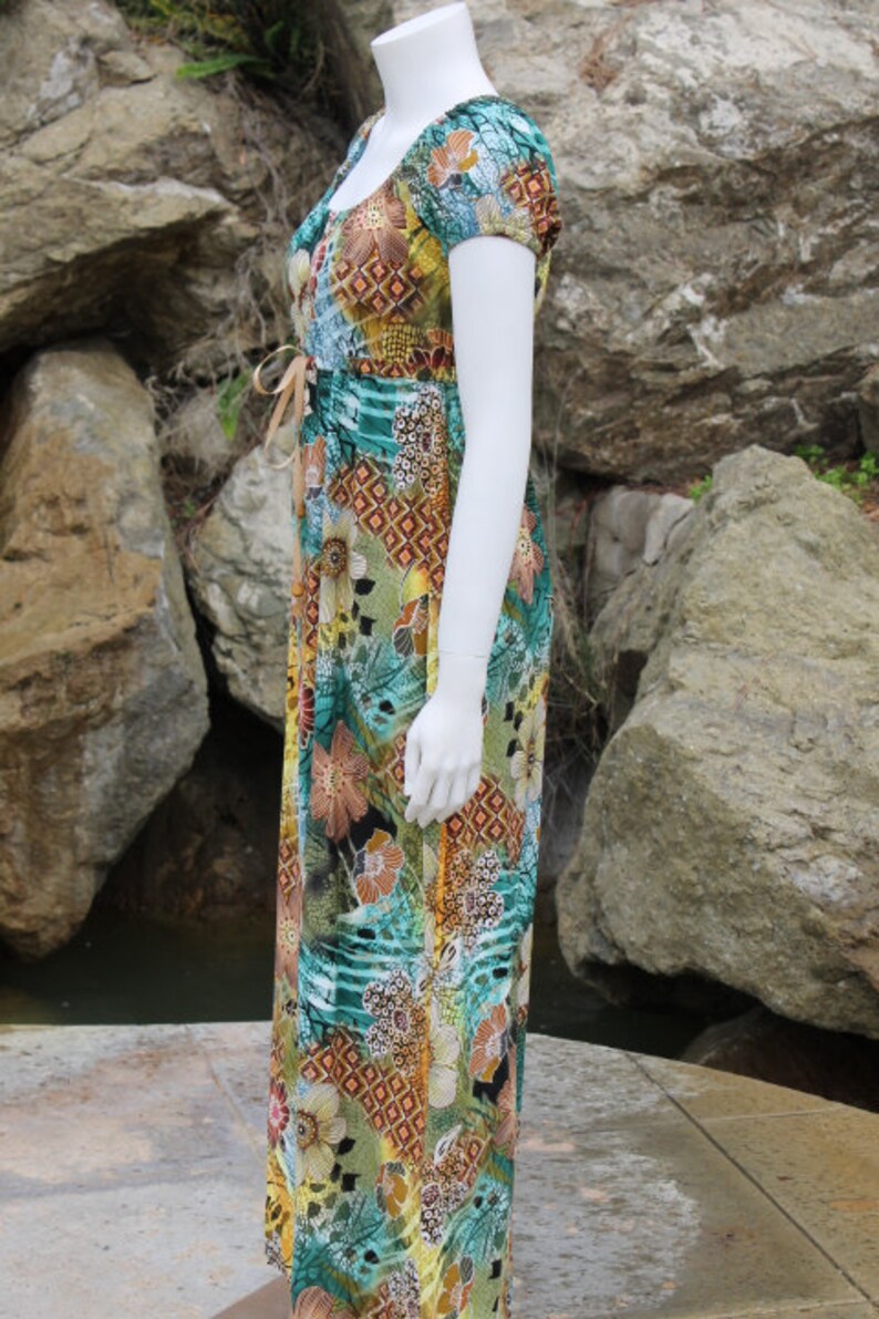 May include: A long, flowing maxi dress with a colorful floral print. The dress has a scoop neck, short sleeves, and a tie at the waist.