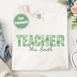 Puede incluir: Sudadera Comfort Colors color crema con la palabra "TEACHER" en letras patchwork verdes. Debajo de la palabra "TEACHER" está el nombre "Mrs. Smith" en una escritura verde oscuro. Un círculo verde con las palabras "Faux Patchwork" está en el lado izquierdo.