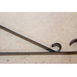 May include: Black metal shelf bracket with a decorative scroll design at the end. The bracket is triangular in shape.