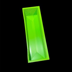 May include: A bright green rectangular container with a textured rim and a geometric design on the bottom. The container is empty and set against a black background.