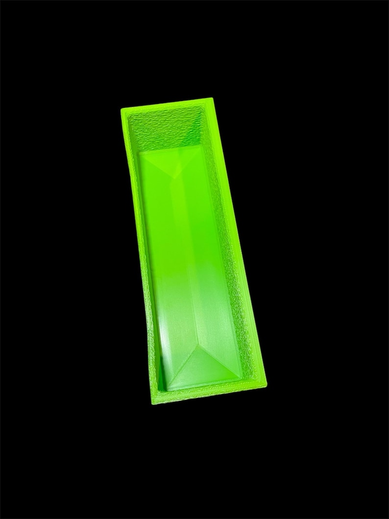 May include: A bright green rectangular container with a textured rim and a geometric design on the bottom. The container is empty and set against a black background.