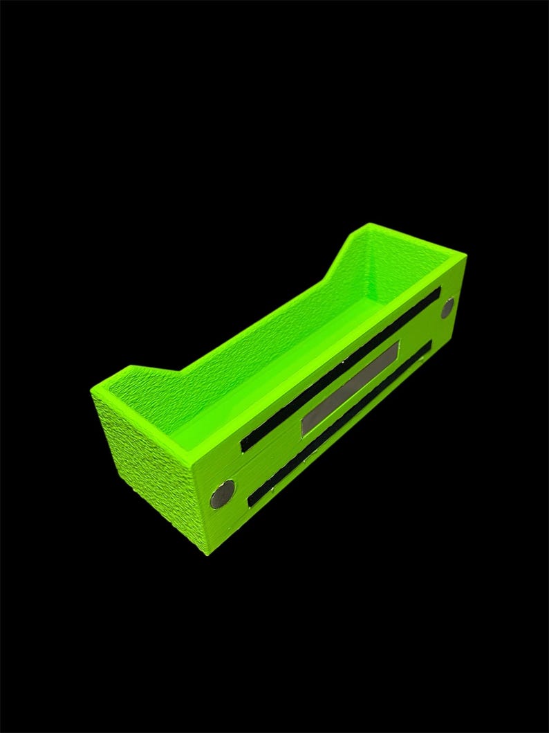 May include: A bright neon green rectangular organizer with a textured surface. The organizer has a tray-like design with raised edges and two black rectangular accents. Two small, round, silver-colored magnets are visible on the side.