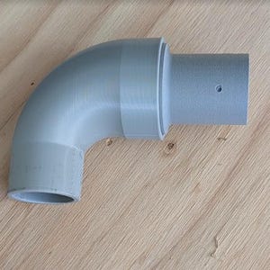 May include: A gray, 90-degree elbow pipe fitting. The fitting is made of plastic and has a smooth, matte finish. It is designed to connect two pipes at a right angle. The fitting is on a wooden surface.