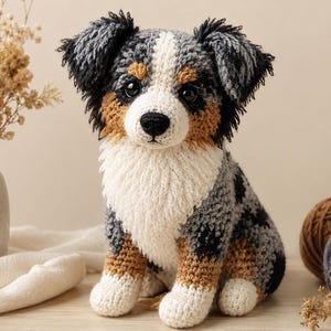 Può includere: Un giocattolo di peluche all'uncinetto a forma di cane con un mantello maculato grigio, nero e marrone, petto e zampe bianche. L'animale ha occhi scuri e rotondi, un naso nero e orecchie testurizzate dall'aspetto arruffato e peloso.
