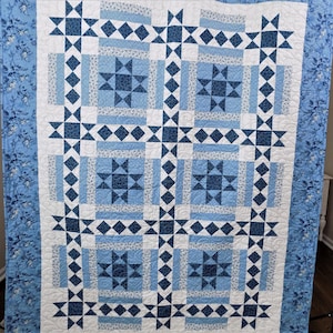 Puede incluir: Una colcha azul y blanca con un patrón de estrellas. La colcha está hecha de diferentes tonos de azul y blanco y tiene un borde de tela floral azul.