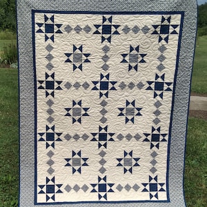Peut inclure: Une courtepointe blanche avec un motif d'étoiles bleu marine. La courtepointe est matelassée avec un motif en spirale et a une bordure bleu marine avec un motif blanc et gris.