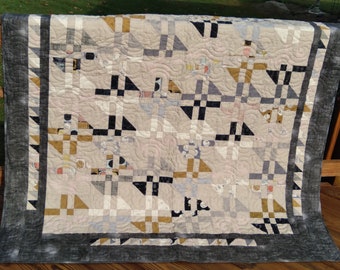 May include: A quilt with a geometric pattern in shades of gray, black, and gold. The quilt is made with a variety of fabrics and has a quilted design.