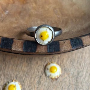 May include: A silver ring with a white and yellow fried egg design.