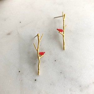 May include: A pair of gold earrings with a small red bird perched on a branch.