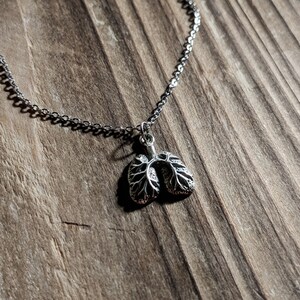 May include: A silver necklace with a detailed anatomical lung pendant. The necklace is on a wooden surface.