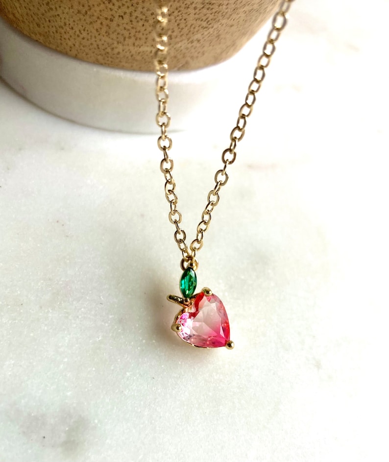 May include: A gold chain necklace with a pink heart-shaped pendant and a green leaf charm.