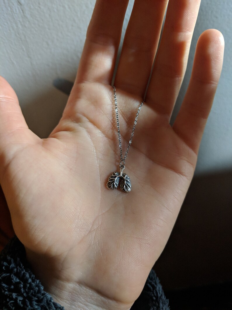 May include: A silver chain necklace with a small, detailed pendant shaped like a pair of lungs.
