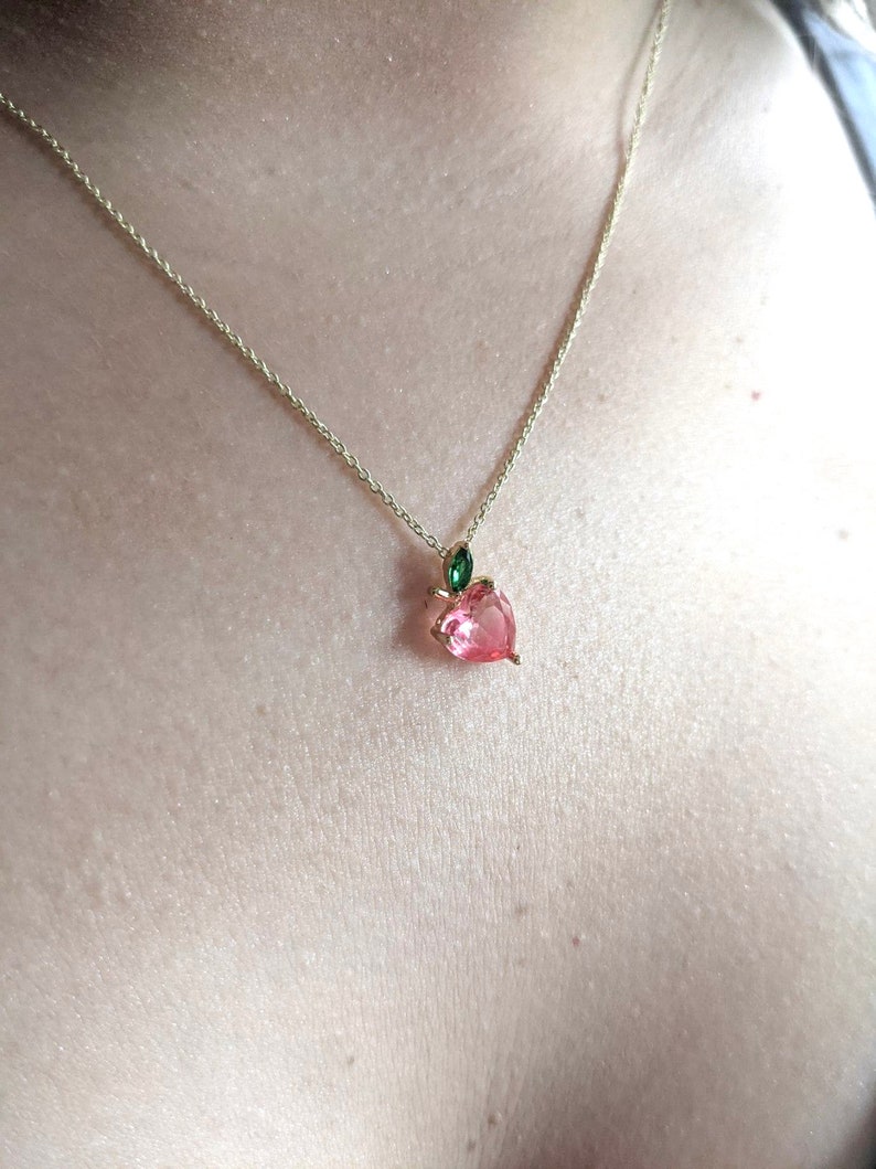 May include: A gold chain necklace with a pink heart-shaped pendant and a green leaf charm.