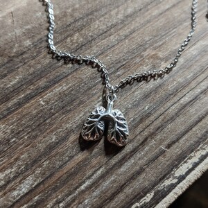 May include: A silver necklace with a detailed anatomical lung pendant. The chain is a simple silver chain.