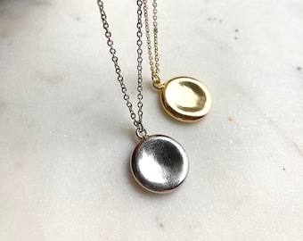 May include: Two silver necklaces with round, flat pendants. One pendant is gold and the other is silver.