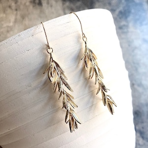 May include: Gold earrings with a delicate design of multiple small leaves hanging from a hook.