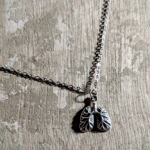 May include: A silver chain necklace with a detailed silver pendant shaped like a pair of lungs.