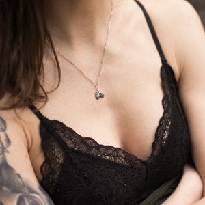 May include: A close-up of a woman wearing a black lace bralette and a silver necklace with a small anatomical heart pendant.