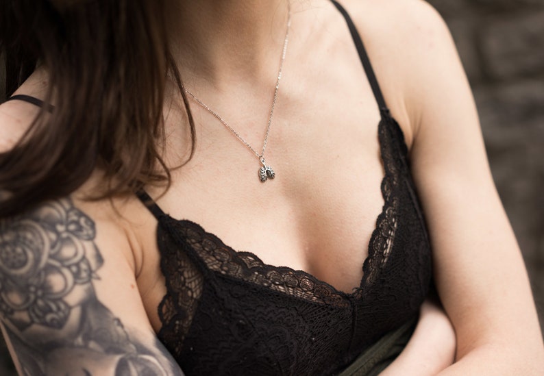 May include: A close-up of a woman wearing a black lace bralette and a silver necklace with a small anatomical heart pendant.