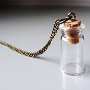 May include: A gold chain necklace with a small glass bottle pendant. The bottle has a cork stopper and is empty.