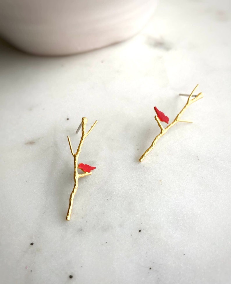 May include: Gold tone earrings with a small red bird perched on a branch.