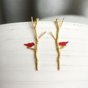 May include: A pair of gold earrings with a red bird perched on each branch. The branches are stylized to look like twigs.