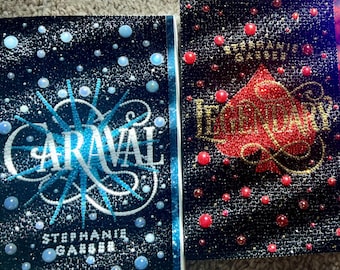 Könnte beinhalten: Drei Hardcover-Bücher mit glitzernden Einbänden. Das erste Buch ist marineblau mit weißen und blauen Akzenten und dem Titel "Caraval". Das zweite Buch ist schwarz mit roten Akzenten und dem Titel "Legendary". Das dritte Buch ist lila mit goldenen Akzenten und dem Titel "Finale".