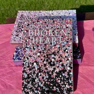 Puede incluir: Dos cajas decorativas con el texto "ONCE UPON A BROKEN HEART" en la parte delantera. Las cajas est&aacute;n cubiertas con un mosaico de cuentas rosas, blancas y negras. Las cajas est&aacute;n sobre una superficie rosa.