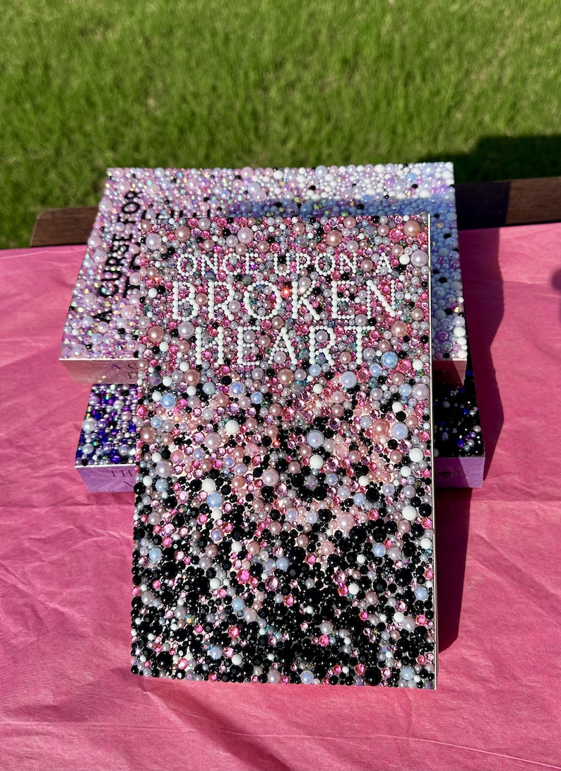 Puede incluir: Dos cajas decorativas con el texto "ONCE UPON A BROKEN HEART" en la parte delantera. Las cajas est&aacute;n cubiertas con un mosaico de cuentas rosas, blancas y negras. Las cajas est&aacute;n sobre una superficie rosa.
