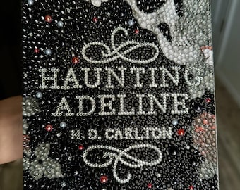 Könnte beinhalten: Ein Buchcover mit dem Titel Haunting Adeline von H. D. Carlton, das vollständig mit kleinen, funkelnden Strasssteinen bedeckt ist. Das Design zeigt einen Totenkopf, Schmetterlinge und dekorative Schnörkel in Schwarz, Weiß und Rot.