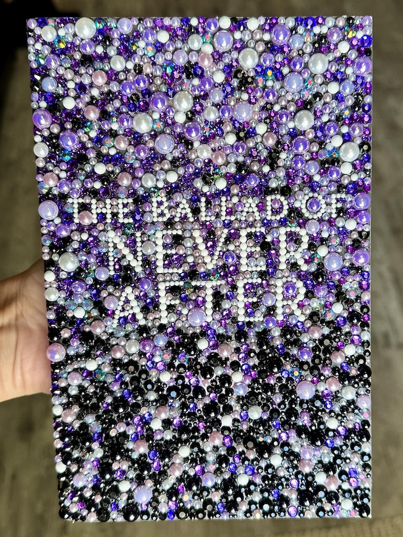 Puede incluir: Una obra de arte rectangular cubierta por un mosaico de cuentas moradas, blancas y negras. El texto "THE BALLAD OF NEVER AFTER" est&aacute; escrito con cuentas blancas. La obra de arte est&aacute; sostenida por una mano.