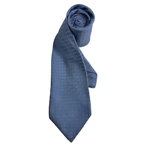 May include: A blue necktie featuring a repeating pattern of small, dark blue letter H symbols across the entire fabric. The necktie is partially rolled at the top, showing the textured weave of the material and the pointed end at the bottom.