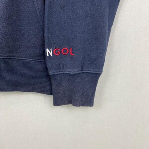 Op de afbeelding: Een marineblauw sweatshirt met lange mouwen, voorzien van een geribbelde boord en zoom. Het woord NGOL is geborduurd in wit en rood garen op de mouw bij de boord. De stof heeft een zichtbare textuur en het kledingstuk heeft een klassieke ronde hals.