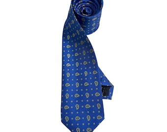 May include: A royal blue necktie featuring a repeating pattern of small gold paisley shapes and tiny square dots. The tie is rolled at the top, showing the interior fabric, and features a pointed bottom end with a visible black label on the back.