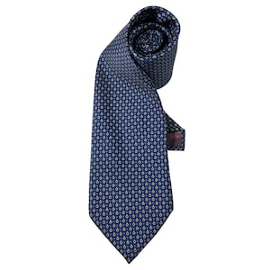 Puede incluir: Una corbata azul oscuro con un patrón repetitivo de pequeños símbolos de botón de encendido en amarillo y azul claro. La corbata está enrollada en la parte superior, mostrando un forro de tela oscura en el reverso, con una punta inferior.
