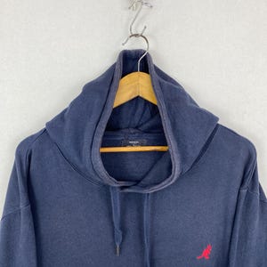 Op de afbeelding: Een marineblauw sweatshirt met capuchon, een hoge kraag en een trekkoord. Het kledingstuk is voorzien van een klein, geborduurd rood kangoeroelogo aan de rechteronderkant en een Kangol-merklabel aan de binnenkant van de kraag.