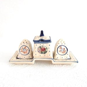 May include: A ceramic salt and pepper set with a matching sugar bowl. The set features a cream-colored base with blue polka dots and hand-painted floral designs. The sugar bowl has a lid with a blue handle.