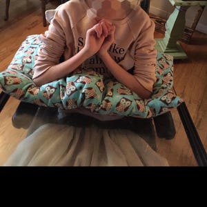 May include: A light brown sweatshirt with the text "S like all my" is visible. A blue pillow with an owl pattern is in the foreground. A light gray tulle skirt is also visible.