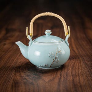 Peut inclure: Une théière en céramique bleu clair avec une anse tressée et un motif floral. La théière a une forme arrondie, un bec verseur et un couvercle avec un petit bouton. La poignée est en matériau tressé clair. La théière est décorée d'un motif floral délicat.