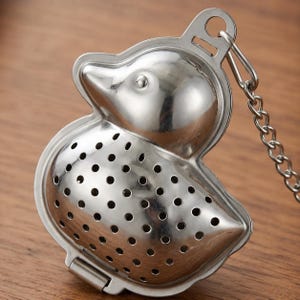 May include: A stainless steel duck-shaped tea infuser with a hinged body and a chain. The infuser has a perforated design for steeping loose leaf tea. The duck's head and body are clearly defined, with a loop for hanging.