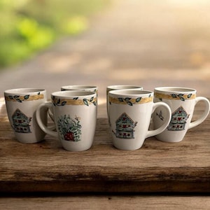 May include: Six white ceramic mugs with a decorative birdhouse and floral design. Each mug has a handle and a yellow and green leaf border. The mugs are arranged on a wooden surface.