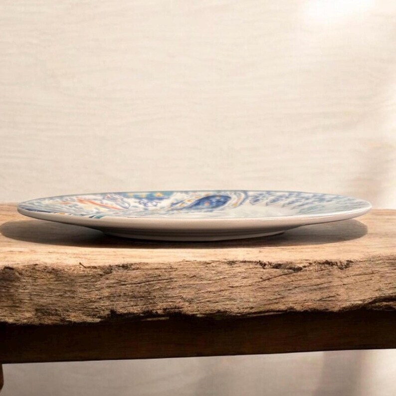 May include: A ceramic plate with a blue and white decorative pattern. The plate is round and has a slightly raised edge. The design includes swirls and floral elements. The plate is resting on a wooden surface.