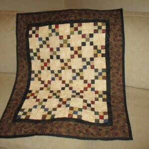 May include: A quilt with a brown, black, and cream colored patchwork design. The quilt has a brown and black border with a floral pattern.