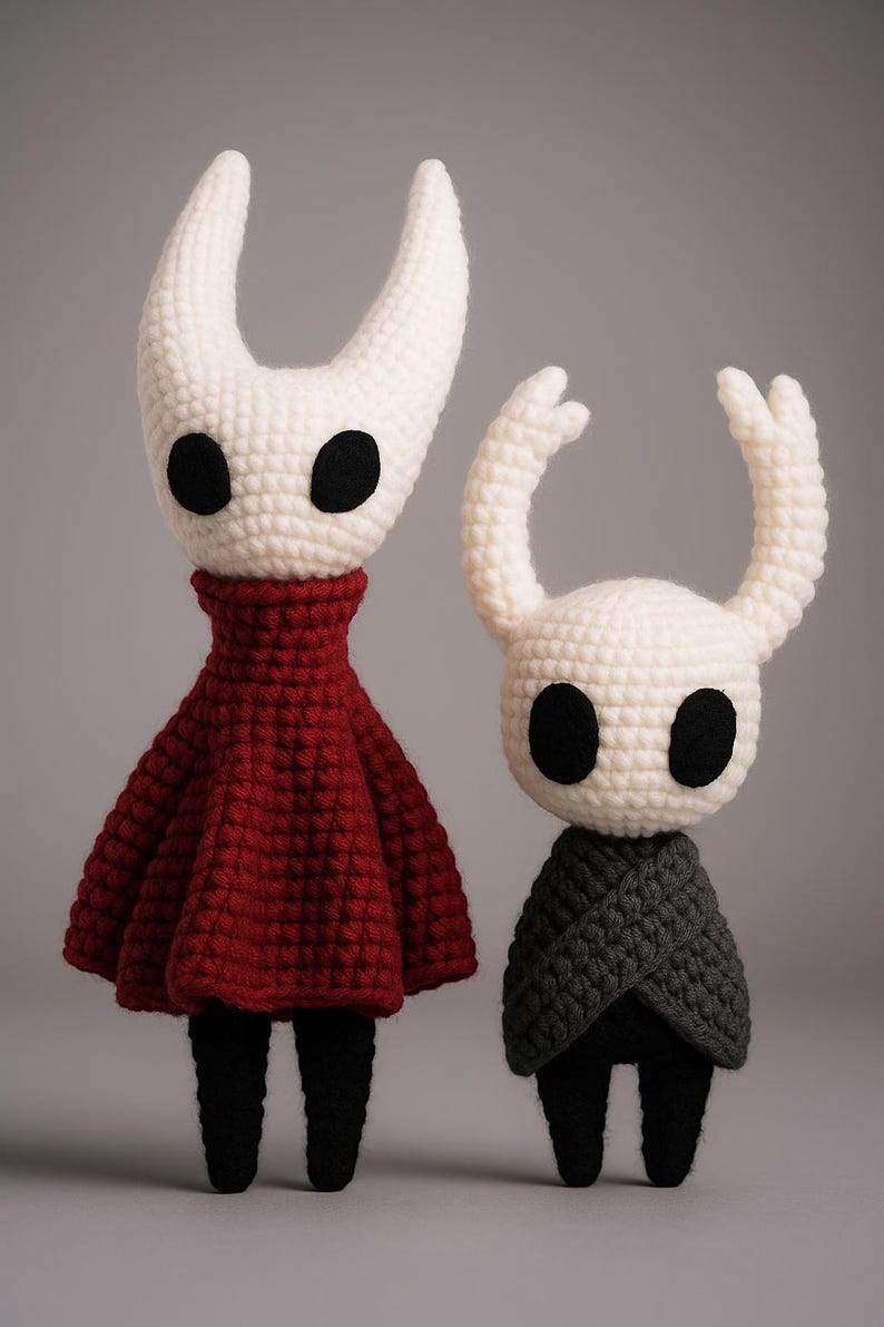 Puede incluir: Dos mu&ntilde;ecos de ganchillo hechos a mano. Uno tiene una cabeza blanca con ojos negros grandes y cuernos curvos, un vestido rojo y piernas negras. El otro tiene una cabeza blanca con ojos negros y cuernos curvos, una capa gris y piernas negras.