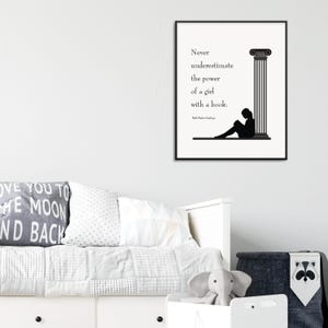 May include: A framed black and white print with the quote, "Never underestimate the power of a girl with a book." The print features a silhouette of a person reading next to a column. The print is displayed above a bed.