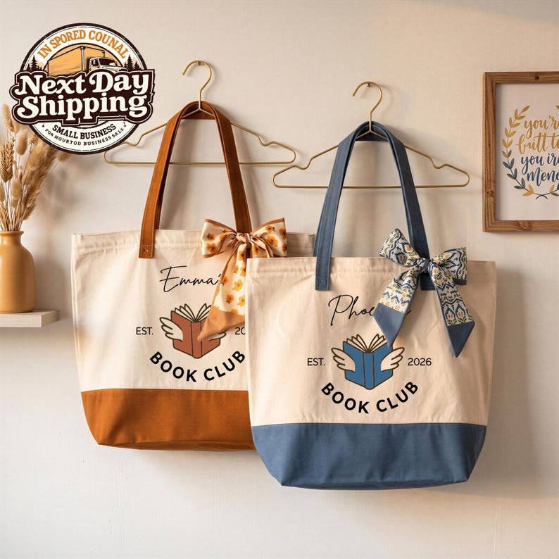 two tote bags hanging on a wall, each with a unique design and color. The bags are displayed on gold hangers, and there is a framed quote in the background.