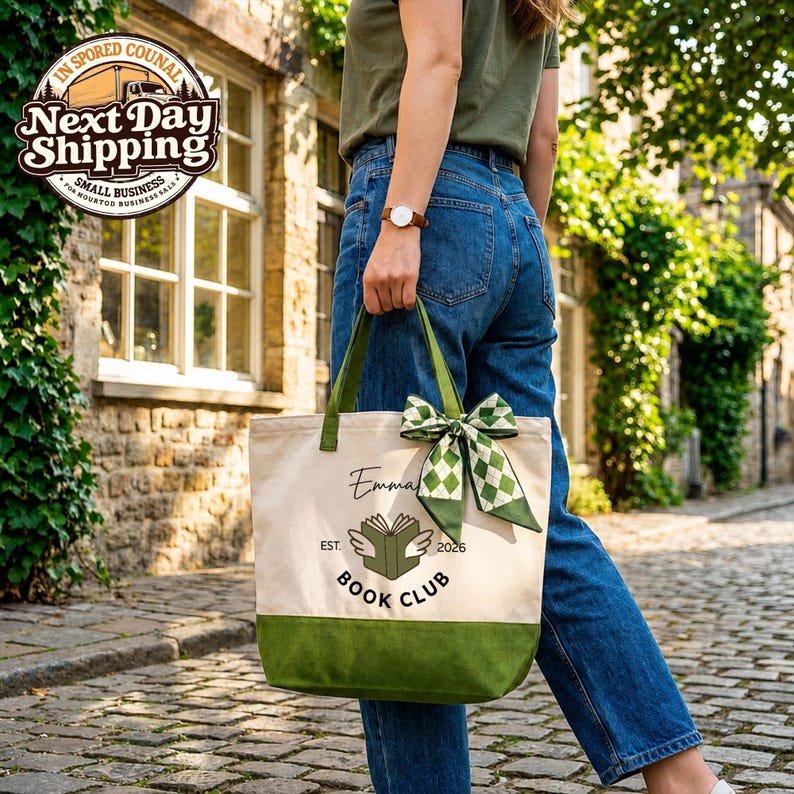 A person is walking down a cobblestone street, carrying a green and white tote bag with a checkered bow and the text "Emma's Book Club" printed on it.