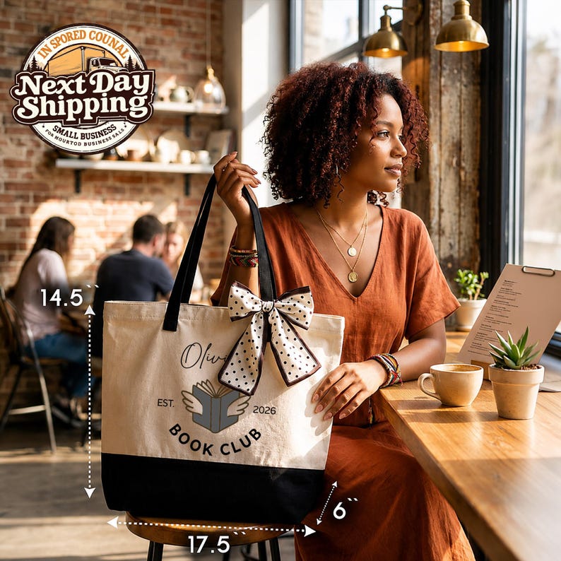 A woman in an orange dress is sitting at a table in a cafe, holding a large tote bag with a book club logo.