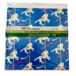 Peut inclure: Papier cadeau bleu avec un motif de chevaux de manège, des poteaux dorés et des rubans colorés. L'emballage porte l'inscription "All-Occasion GIFT WRAP" et la marque "CLEO". Le papier est couché et épais.